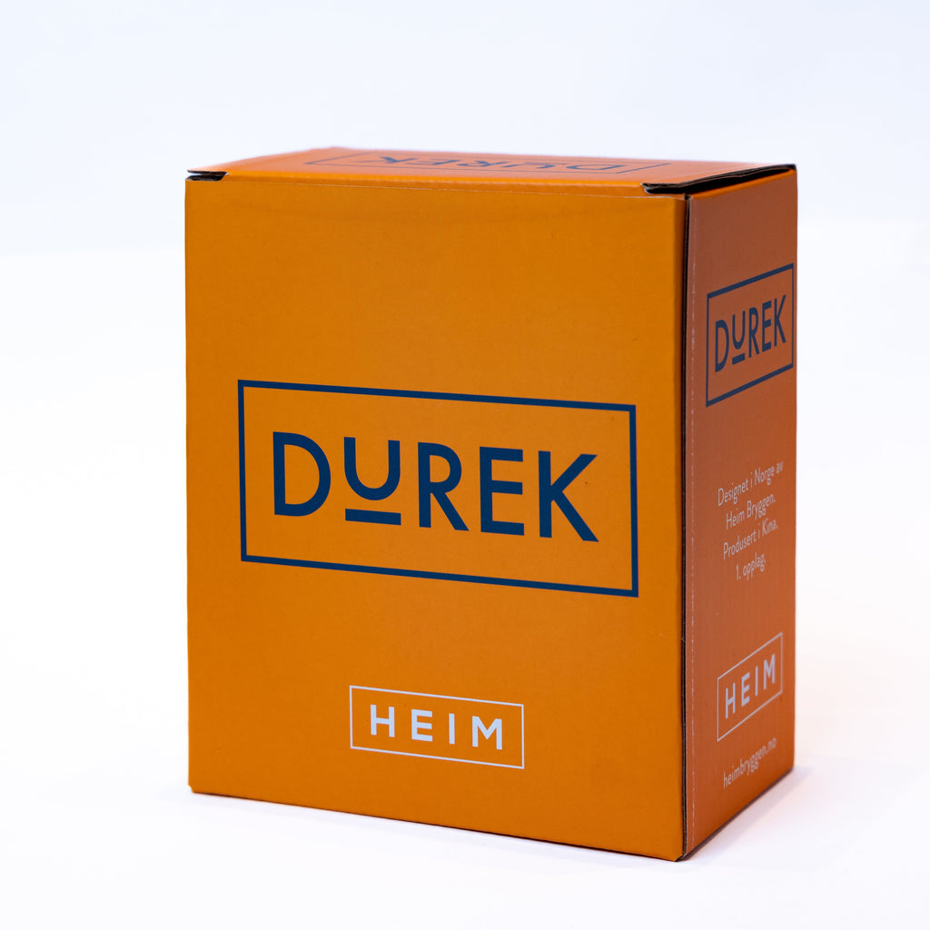 MÄRTHA OG DUREK Julekule - By HEIM Studio i oransje eske med blå tekst og moderne design for unik julepynt