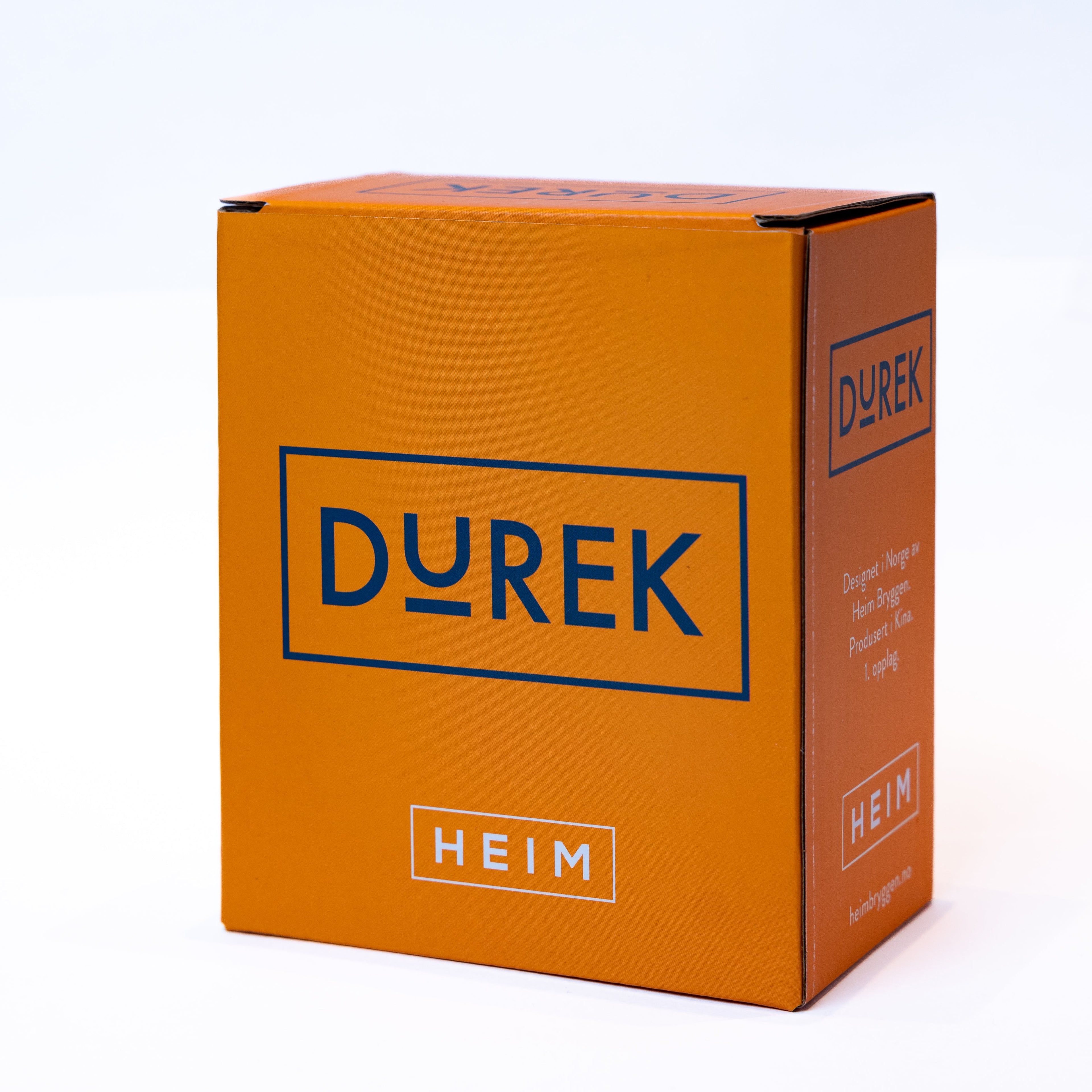 MÄRTHA OG DUREK Julekule - By HEIM Studio i oransje eske med blå tekst og moderne design for unik julepynt